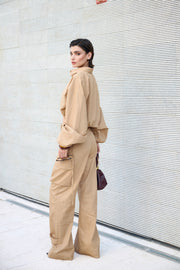 Woman in a beige outfit standing against a light-colored wall.